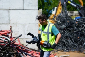 Worker holding a Holmatro handheld hydraulic shear at a cable pile