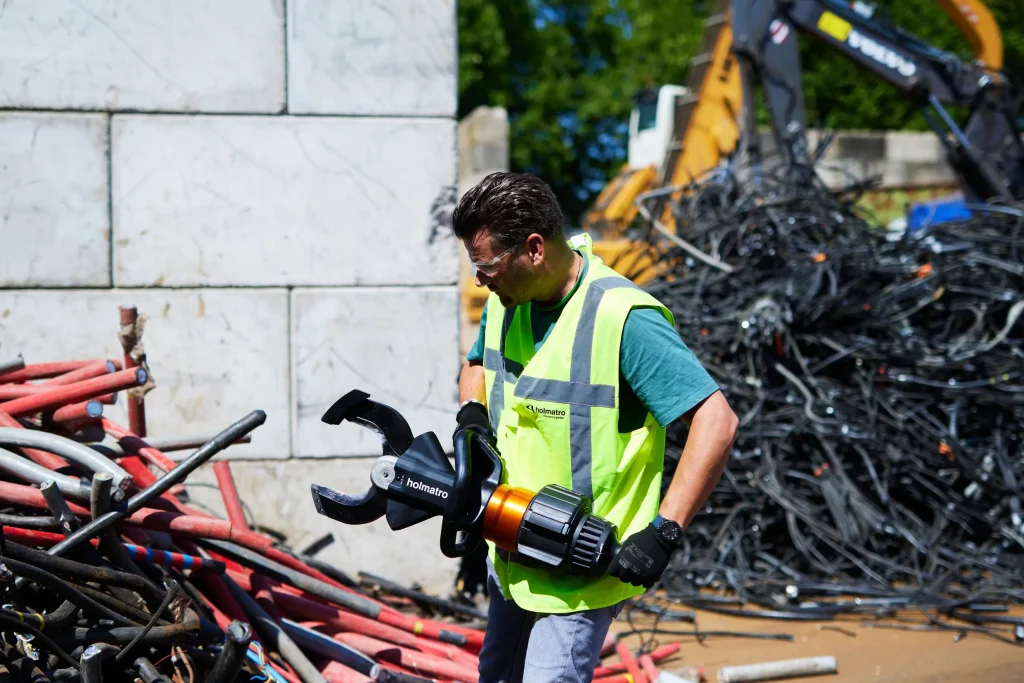 Worker holding a Holmatro handheld hydraulic shear at a cable pile